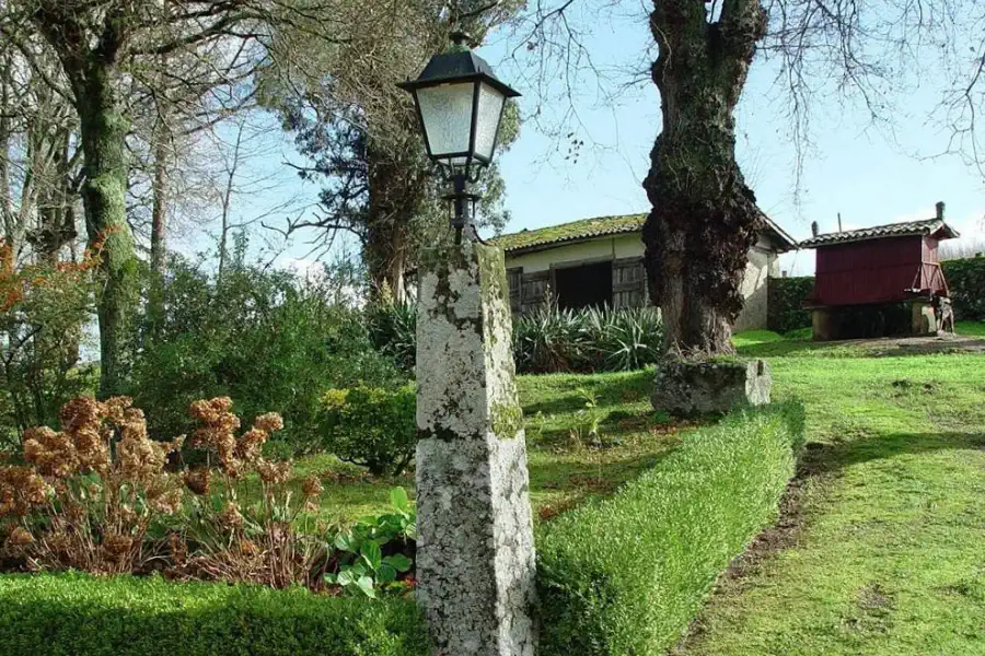 Giardino con lanterna in pietra, edificio secondario e hórreo galiziano sullo sfondo.